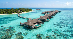 Aerial view of overwater villas extending into turquoise lagoon, Maldives, bright midday sun, crystal-clear water showin